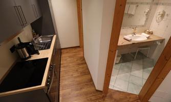 A modern kitchen with wood accents and elegant appliances. Right next to it is a bright bathroom with a sink and towels.