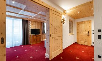 A cozy hotel room entrance with wood paneling and a red carpet. On the left side, a television is visible, and there are windows with curtains.