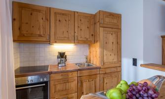 A cozy wooden kitchen with modern appliances. On the countertop, there is a fruit bowl with apples and grapes.