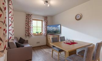 A bright and inviting living space with a table and chairs. Next to a window stands a television, and there is a cozy couch.