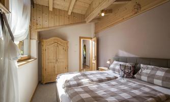 A cozy bedroom with a double bed and checkered blankets. The room has wooden ceilings and a wooden wardrobe, along with a window with curtains.
