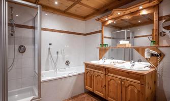 A modern bathroom with a shower, a bathtub, and a wooden vanity. The walls are bright, and the ceiling is made of wood, creating a cozy atmosphere.
