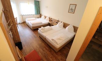 A comfortable room with two single beds and a double bed. The room has bright walls, wooden flooring, and plenty of daylight.