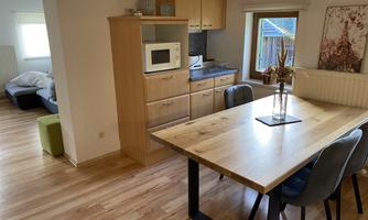 A cozy living kitchen with a wooden table and chairs. In the background, a refrigerator and a microwave are visible.