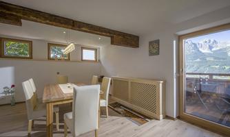 An inviting dining area with a wooden table and bright chairs. Large windows offer a view of the surrounding landscape.