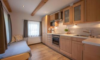 A modern kitchen with light wood cabinets and stainless steel appliances. A cozy seating area with a window provides daylight.