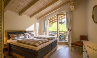 A cozy bedroom with a double bed and wooden ceiling. Large windows offer a view of nature.
