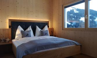 A cozy bedroom with wood paneling and a large window. The bed is modern and inviting, with beautiful pillows.