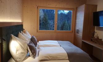 A cozy bedroom with a double bed and large windows. Outside, you can see a green landscape.