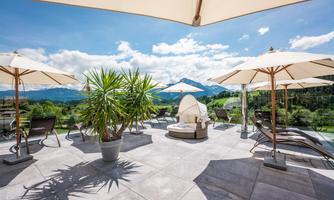 A stylish terrace with loungers and sun umbrellas. In the background, green mountains and a blue sky can be seen.