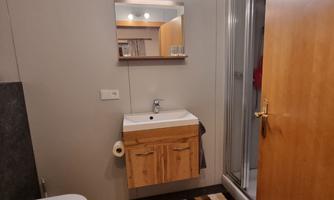 A modern bathroom with a shower, a sink, and a mirrored cabinet. The floor is decorated with a striped rug and a green doormat.