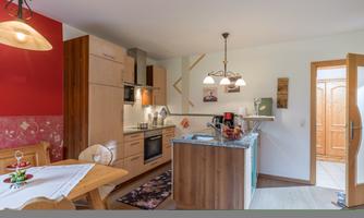A modern kitchen with wooden cabinets and an elegant dining table. The walls are designed in warm colors, and there is pleasant lighting.