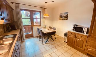 A cozy kitchen with wooden cabinets and a dining table.  
Plenty of light filters through the windows, creating an inviting atmosphere.