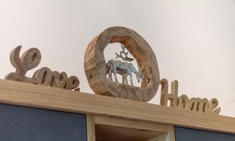 A decorative wooden sculpture featuring the words "Love" and "Home". In the center is a shaped deer within a circular wooden frame.