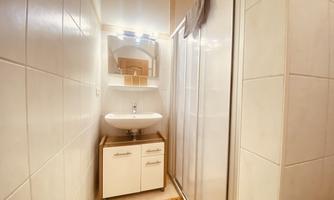 A modern bathroom with a shower, a sink, and a mirror. The walls are tiled and there is a wooden floor.
