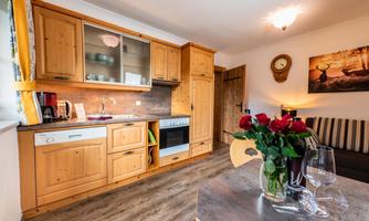 A cozy kitchen with wooden cabinets and modern amenities. On the table, there is a vase of roses and glasses that look inviting.
