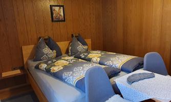 A cozy bedroom with a double bed and blue bedspreads. On the right, there is a small table with chairs.