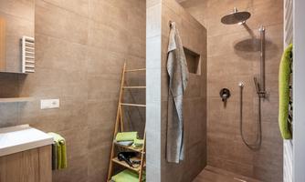 A modern bathroom with a shower and gray tiles. Towels and green bathroom accessories are neatly arranged on a rack.
