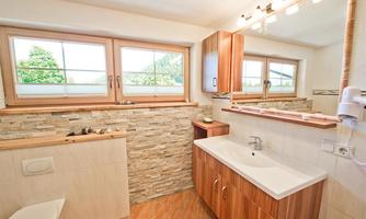 A modern bathroom with wood and stone accents. Bright windows let in plenty of daylight.