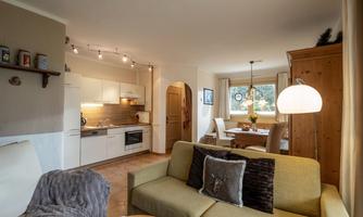 A cozy living space with a modern kitchen and a dining area. The sofa and the wooden cabinet give the room a warm atmosphere.