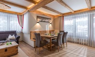 A bright living area with a wooden ceiling and large windows. The room includes a dining table and a cozy seating area.