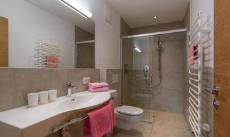 A modern bathroom with a shower and a simple sink. Pink towels and a bright, friendly atmosphere characterize the space.