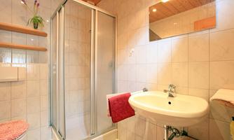 A modern bathroom with a shower cabin and a sink. It is bright and friendly, with tiled walls and wood details.