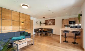Modern apartment with an open living kitchen and a cozy living area. The space is bright and friendly designed, with wooden and green accents.