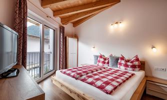 A cozy bedroom with a large bed and checkered bedspreads. Bright walls and a wooden ceiling create an inviting atmosphere.