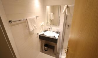 A small bathroom with a sink, a mirror, and towels hanging on the wall. The room is bright and designed in a modern style.