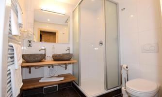 A modern bathroom with a glass shower and double sink. There are bright walls and elegant wooden details.
