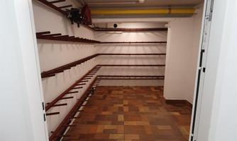 An empty basement room with brown tiles and shelves along the walls. The ceiling is illuminated by a ceiling light.