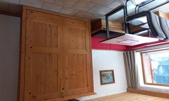 A cozy room with a wooden cabinet and a table with chairs. The walls are bright, and a window lets in plenty of daylight.