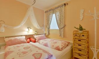 A cozy bedroom in soft pastel colors. It features two beds with heart patterns and a decorative dresser.