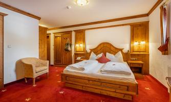 A cozy bedroom with wooden furnishings and a red carpet. The bed is decorated with white bed linen and pillows.