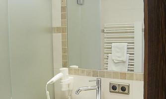 A modern bathroom with two sinks and a large mirror. The shower cubicle is made of glass and there are towels next to the radiator.