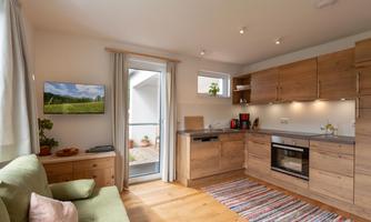 A modern kitchen with wooden cabinets and bright surfaces. A cozy sofa and a window create an inviting atmosphere.