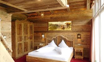 A cozy bedroom with wooden furnishings and a large bed. There is a wardrobe and a window that provides plenty of daylight.