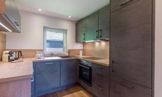 A modern kitchen with wooden surfaces and elegant cabinets. Bright light flows through the window, creating an inviting atmosphere.