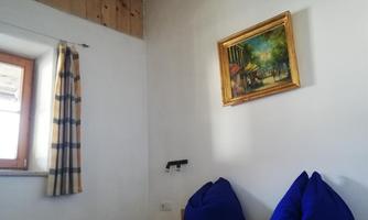 A cozy bedroom with light walls and a wooden ceiling beam. Two blue cushions and a painting on the wall complete the tranquil atmosphere.