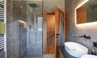 A modern bathroom with a glass shower and an elegant sink. The walls are designed in a grey stone decor, and there is warm wood for a cozy touch.
