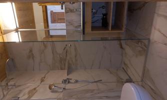 A modern bathroom with marbled walls and a glass shower. The wooden details give the space a warm atmosphere.