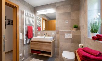 A modern bathroom with warm wood elements and stone tiles. Red towels and a large plant give the space an inviting atmosphere.