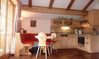 A cozy kitchen with wooden paneling and a dining area for four people. Large windows provide plenty of daylight and a friendly atmosphere.