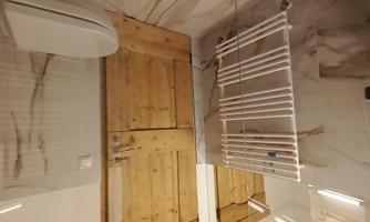 A modern bathroom with wood and marble elements. The image shows a shower, a toilet, and a towel holder.