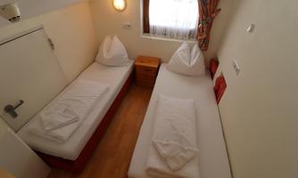 A simple room with two single beds and a window. The walls are bright and there is a small wooden wardrobe.