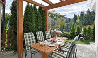 An inviting outdoor dining area with a wooden table and several chairs. Surrounded by green trees and a beautiful view of the mountains.