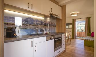 A modern kitchen with white cabinets and wooden fronts. In the background, there is a landscape with mountains and water.