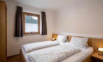 A cozy bedroom with a double bed and two nightstands. The window lets in soft light and offers a view outside.