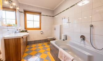 A modern bathroom with a shower and bathtub. The floor tiles are in yellow and gray, and there are large windows that let in plenty of light.